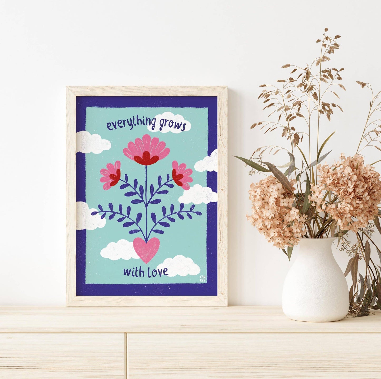 Affiche murale colorée avec des fleurs, des nuages et un message positif dans un cadre en bois.