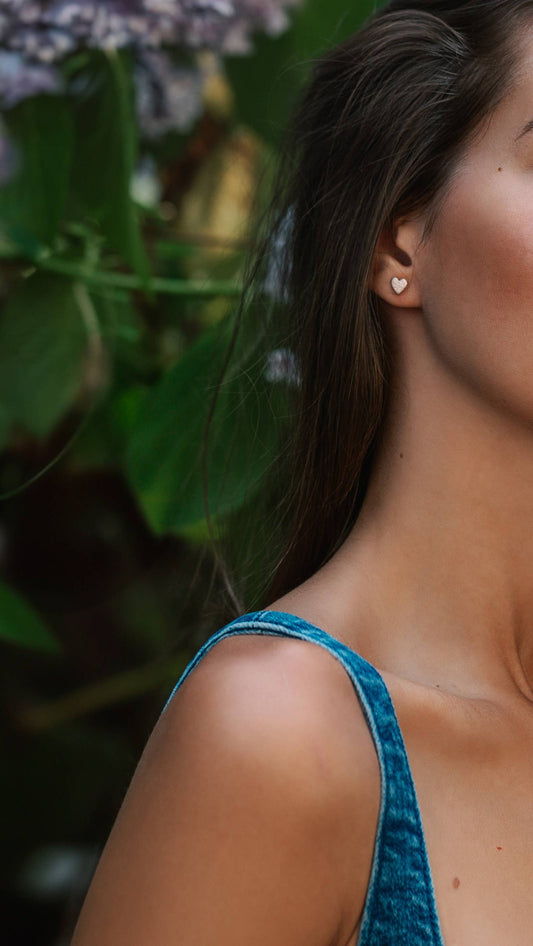 Boucles d'oreilles en cuir upcyclé en forme de cœur rose irisé, portées par une femme brune.