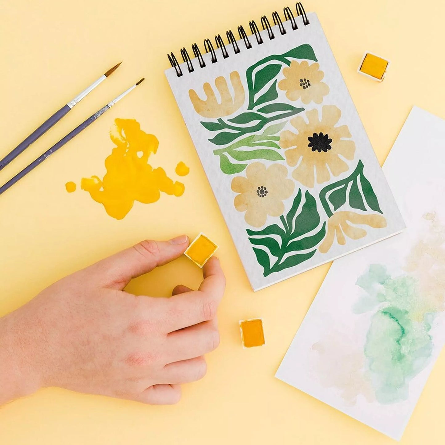 carnet de coloriages pour adultes avec des fleurs, des pinceaux et de la peinture jaune.
