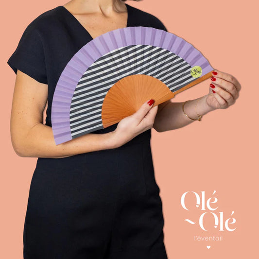 Éventail en bois fabriqué en Espagne, couleur mauve, blanc et noir, porté par une femme.