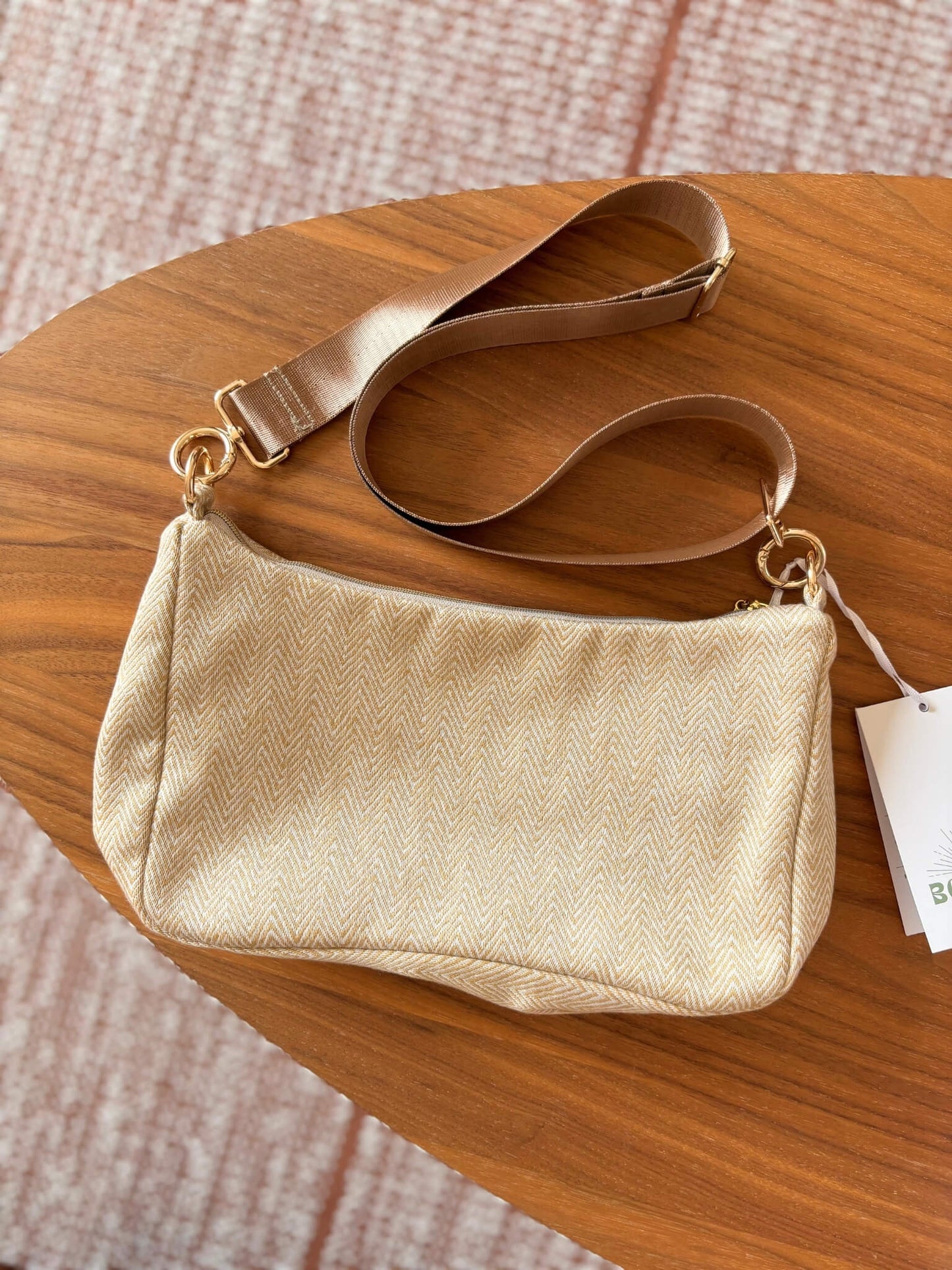 Sac baguette beige en coton, avec une sangle mordorée réglable.