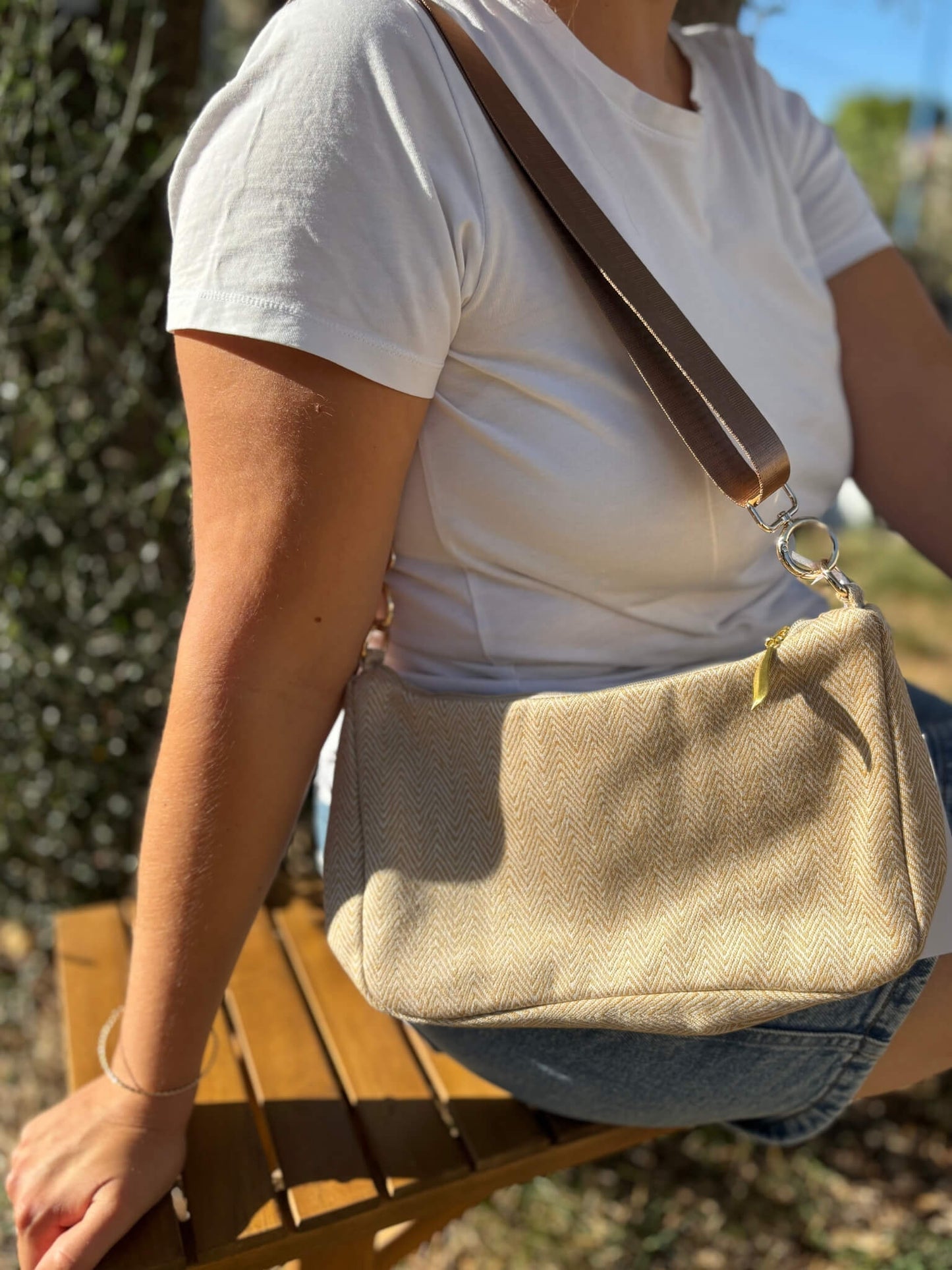 Sac baguette beige en coton, avec une sangle mordorée réglable.
