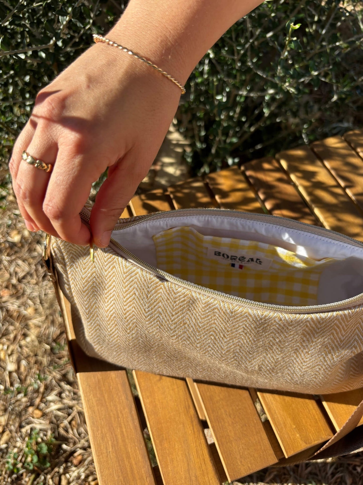 Sac baguette beige en coton, avec une sangle mordorée réglable.
