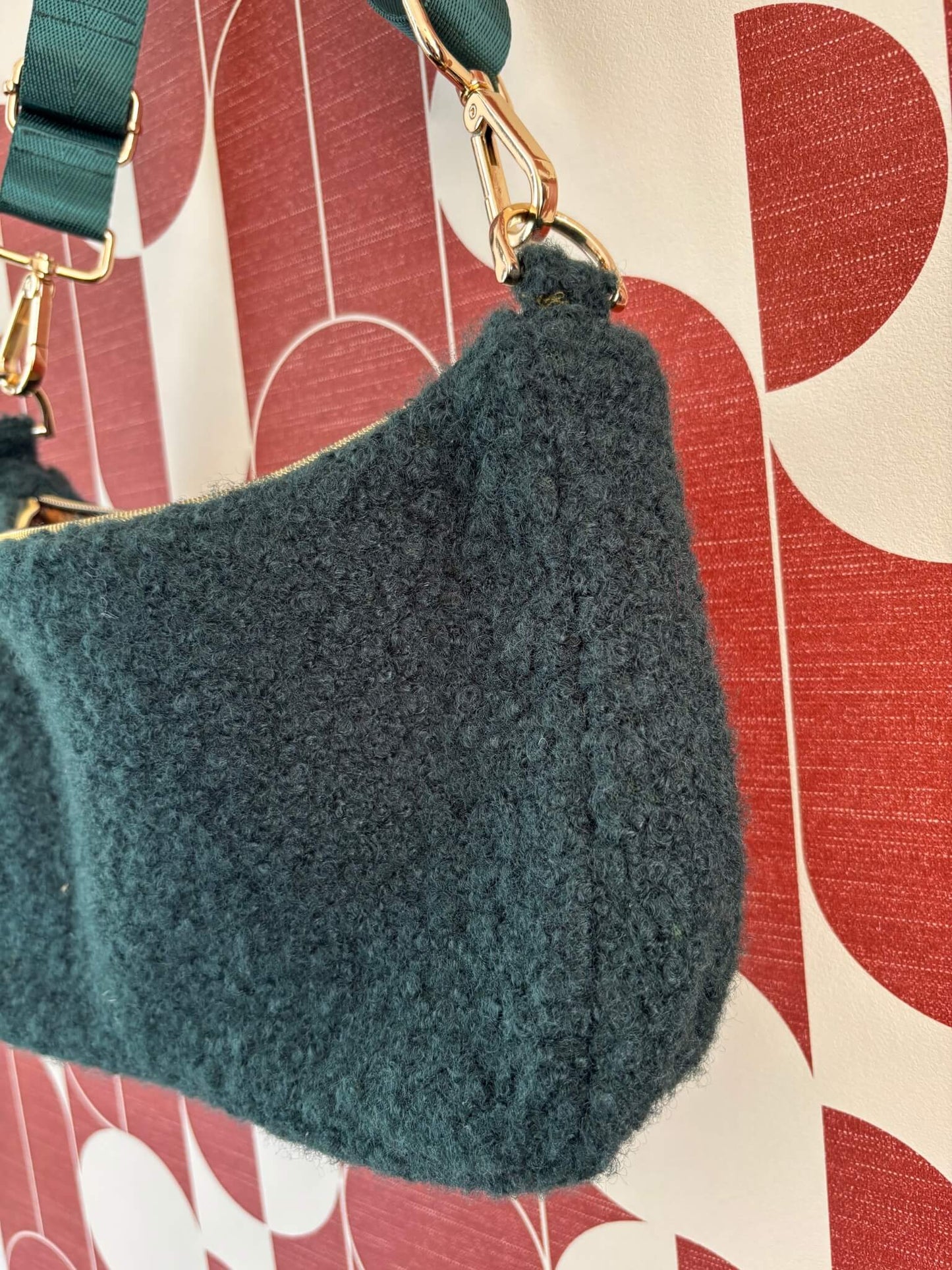 Sac baguette en moumoute verte accroché à une patère dorée.