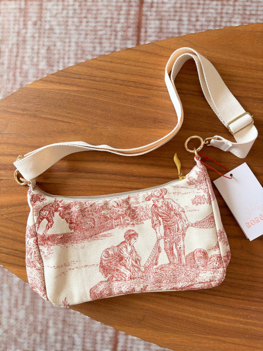 Sac baguette en toile de Jouy rouge, avec une sangle beige réglable.