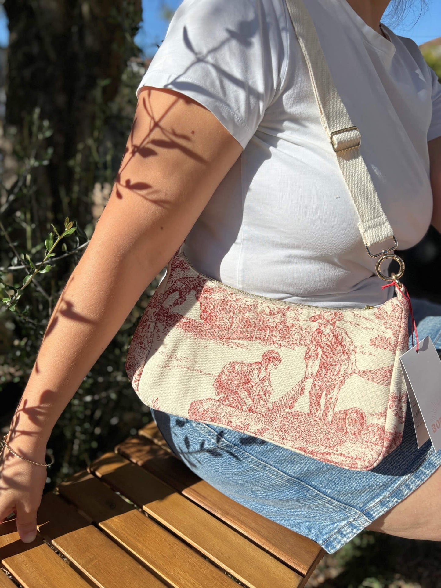 Sac baguette en toile de Jouy rouge, avec une sangle beige réglable.