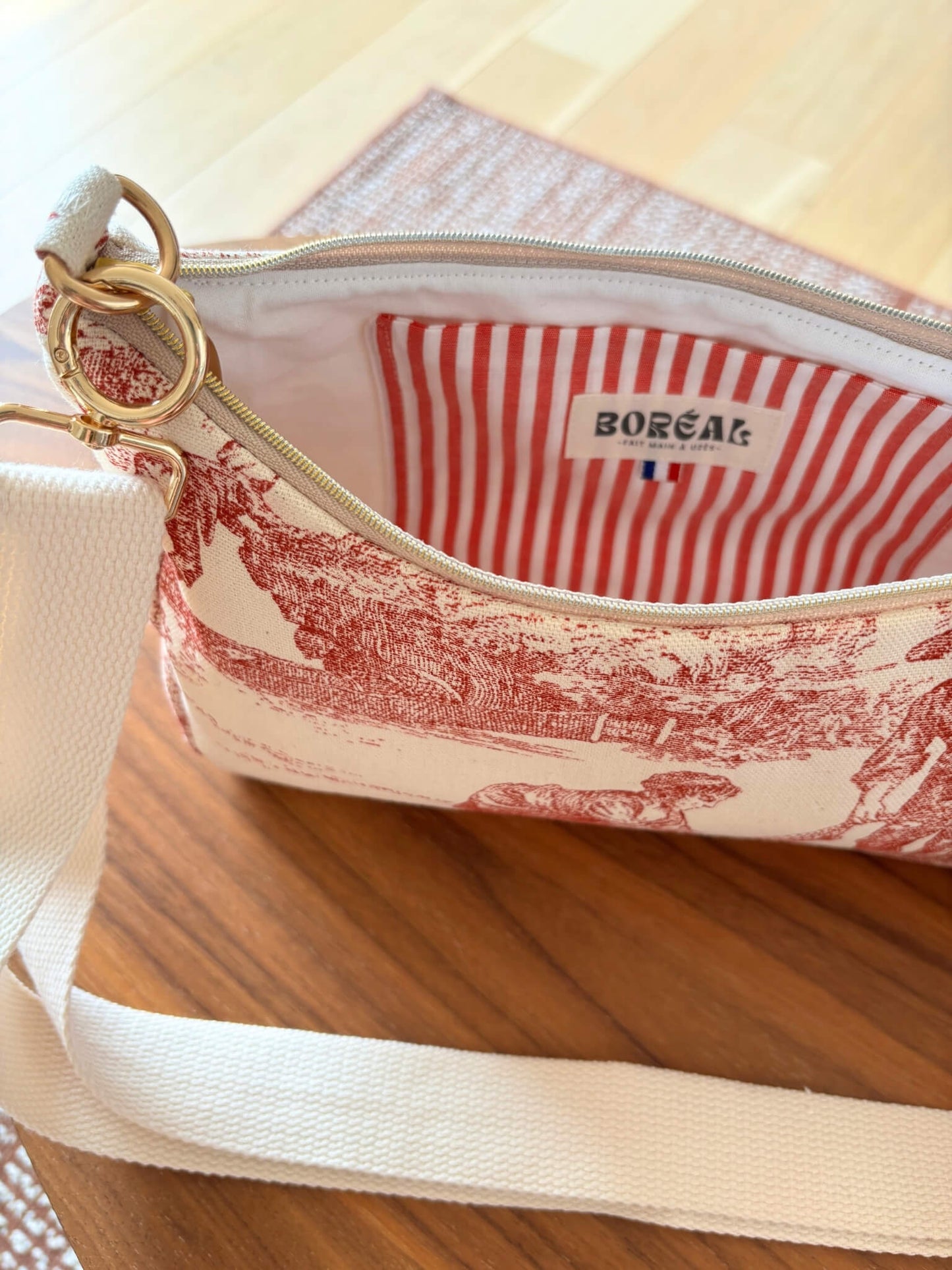 Sac baguette en toile de Jouy rouge, avec une sangle beige réglable.