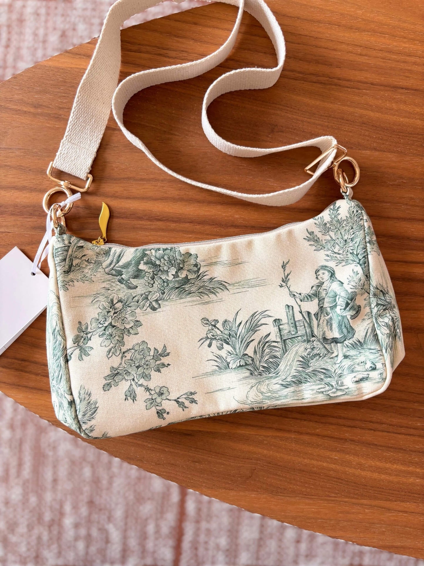 Sac baguette en toile de Jouy verte, avec une sangle beige réglable.