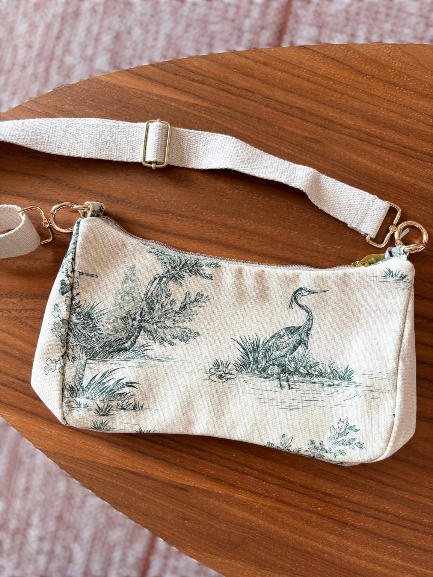 Sac baguette en toile de Jouy verte, avec une sangle beige réglable.
