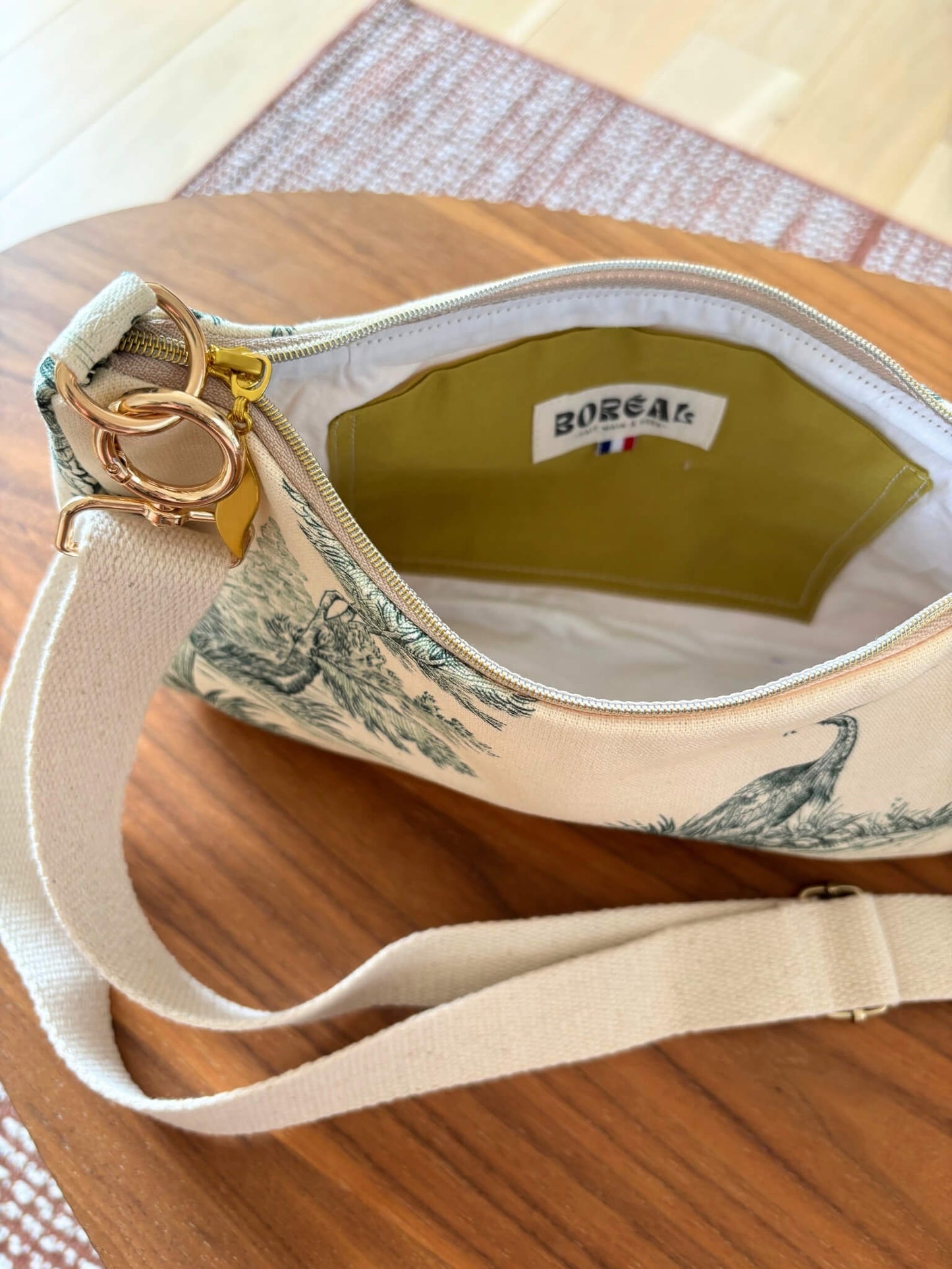 Sac baguette en toile de Jouy verte, avec une sangle beige réglable.