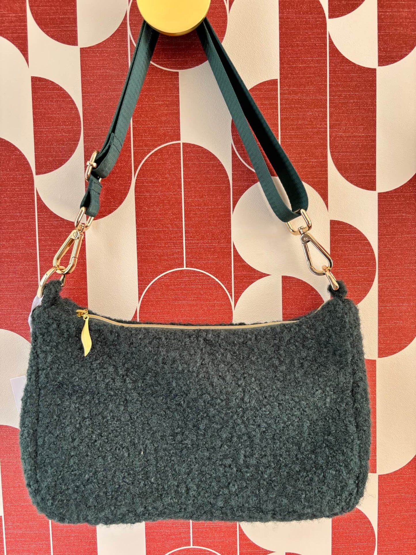 Sac baguette en moumoute verte accroché à une patère dorée.