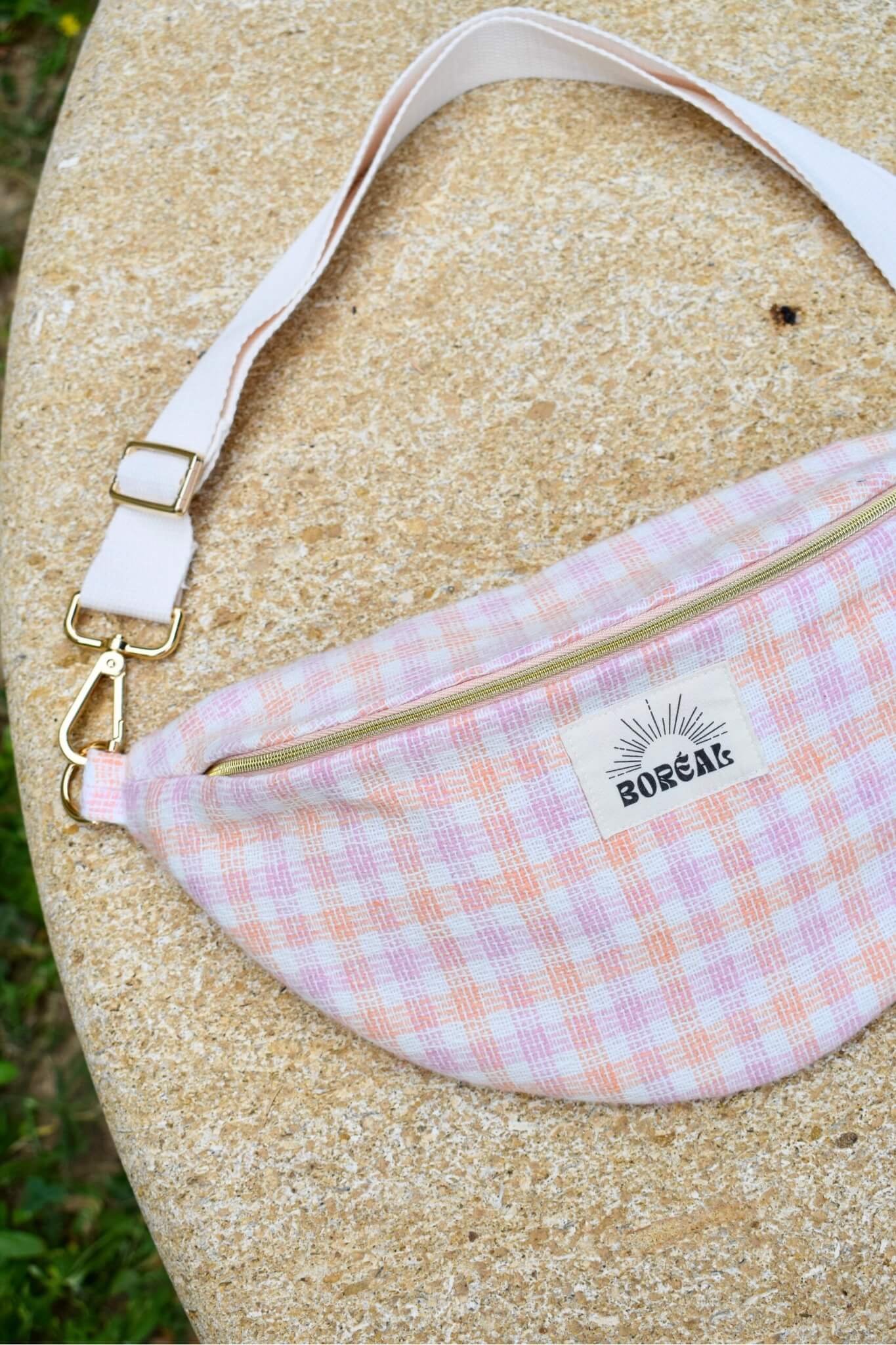 Sac banane upcyclé, à carreaux rose et orange, posé sur un banc en pierre.