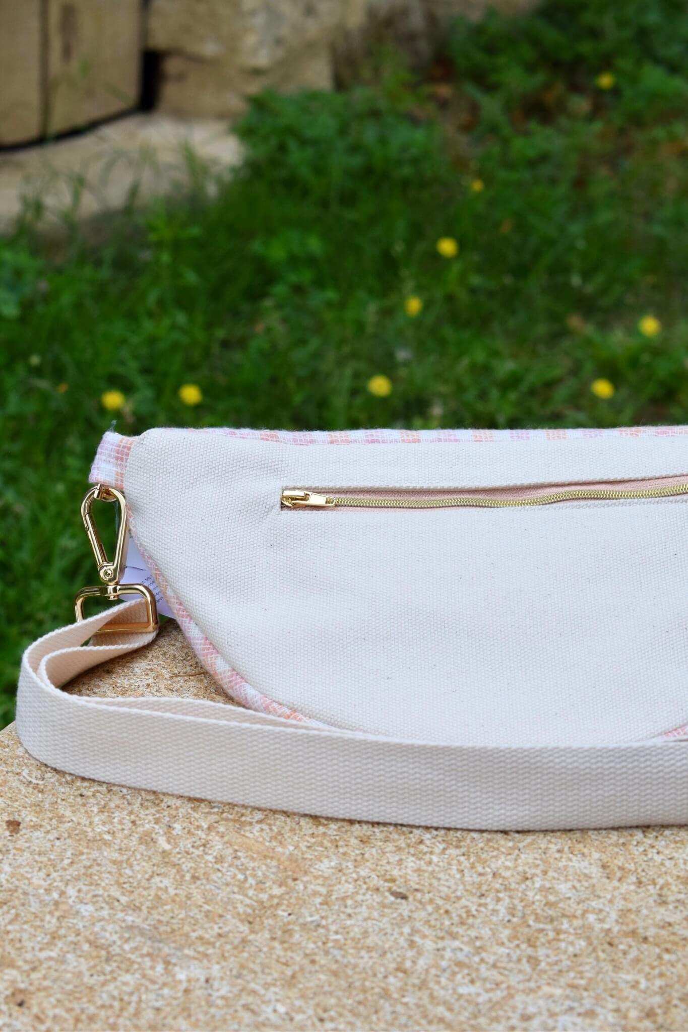 Sac banane upcyclé, à carreaux rose et orange, posé sur un banc en pierre.