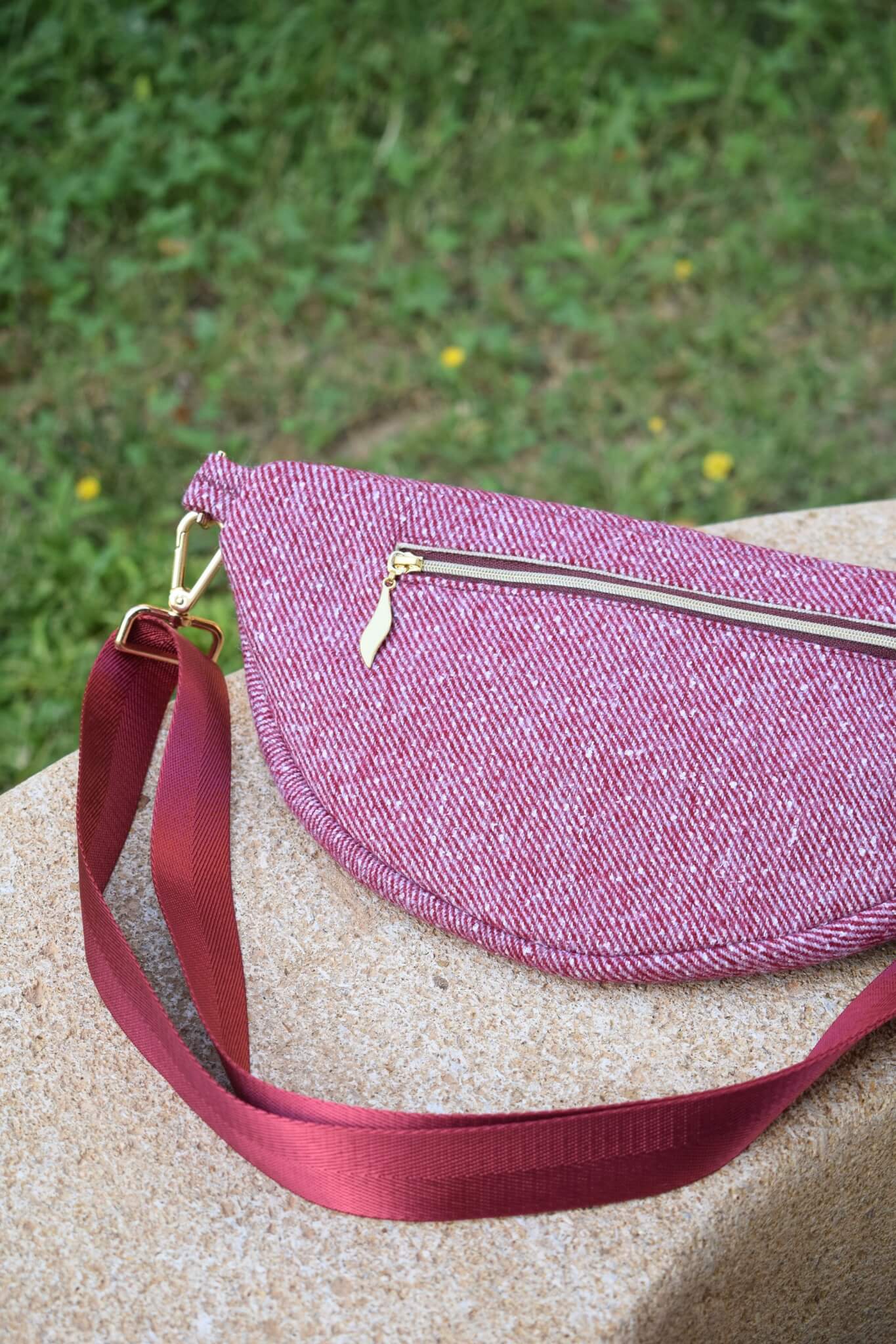 Sac banane upcyclée rouge et dorée en laine, posé sur un banc en pierre