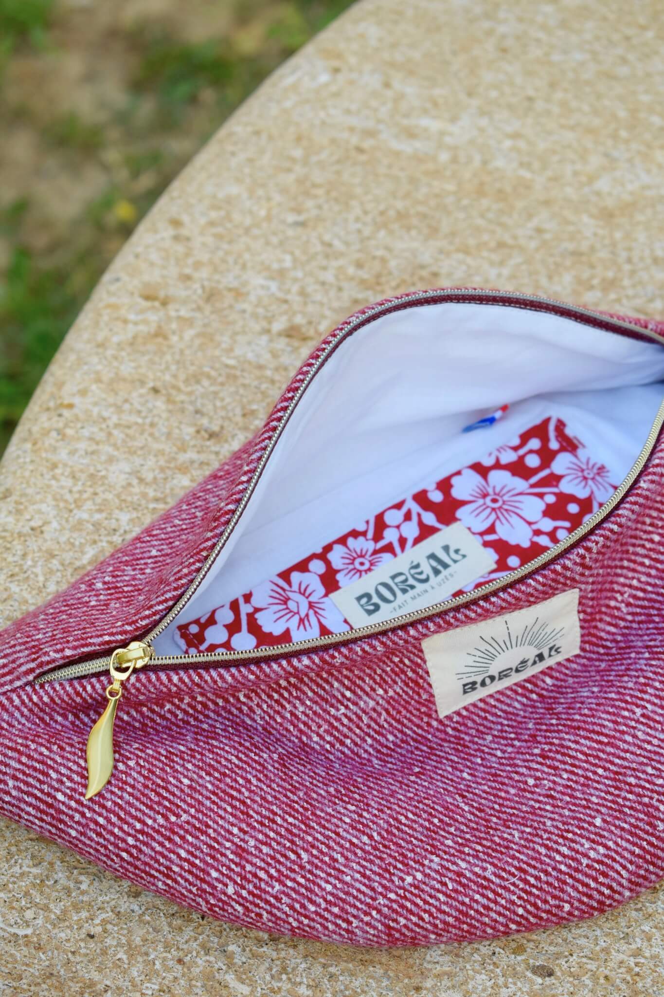Sac banane upcyclée rouge et dorée en laine, posé sur un banc en pierre