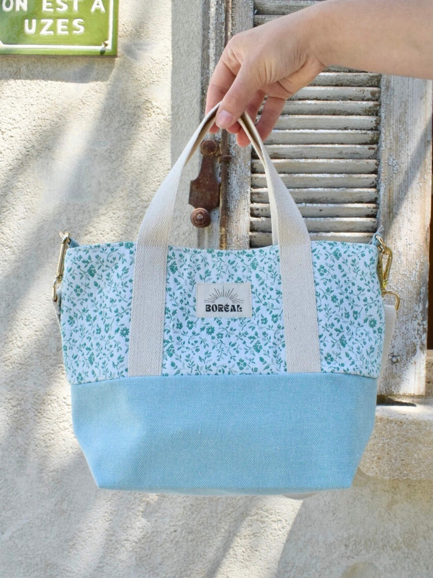 Sac à bandoulière en coton bleu fleuri, avec une sangle beige réglable.