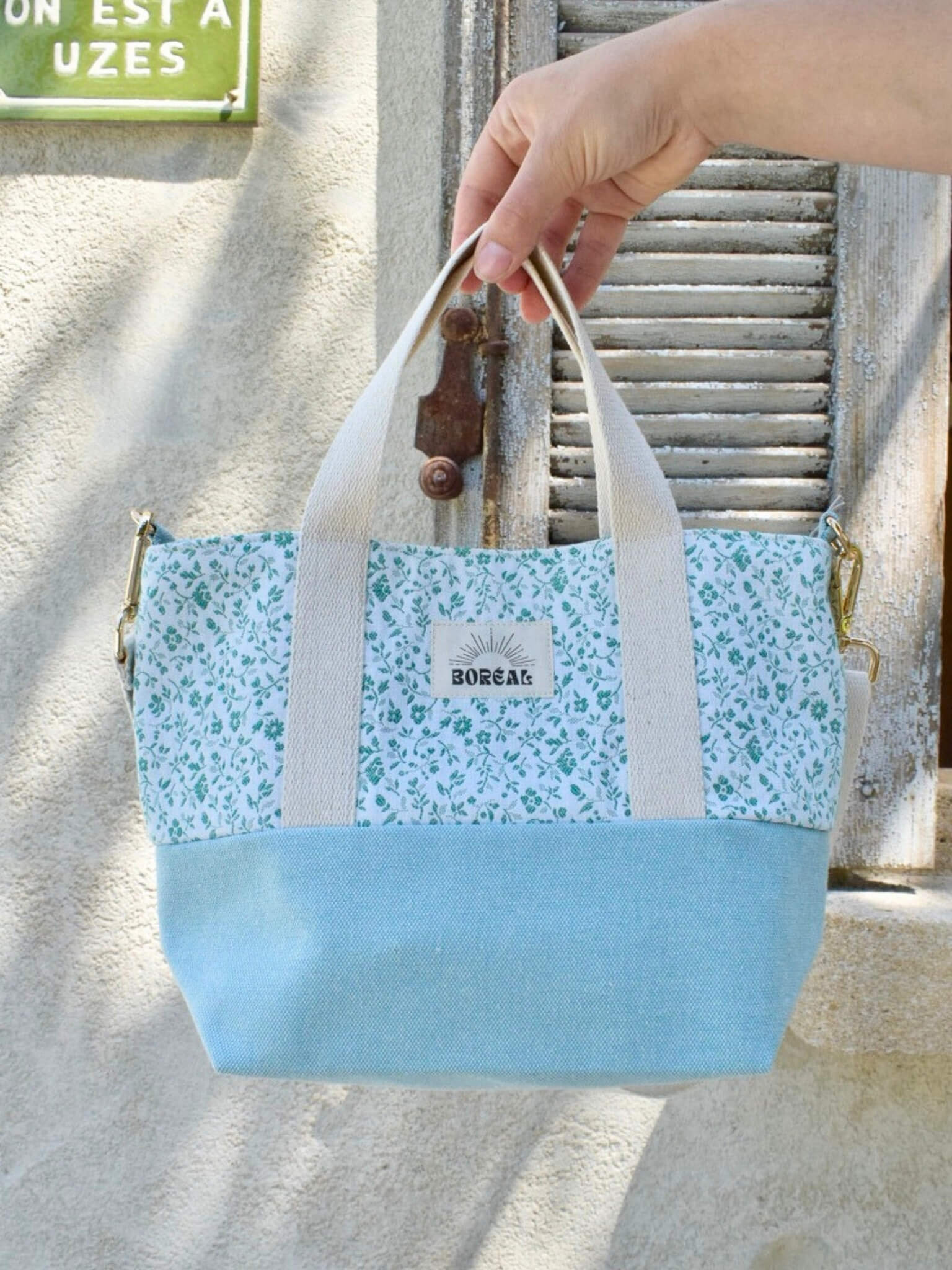 Sac à bandoulière en coton bleu fleuri, avec une sangle beige réglable.