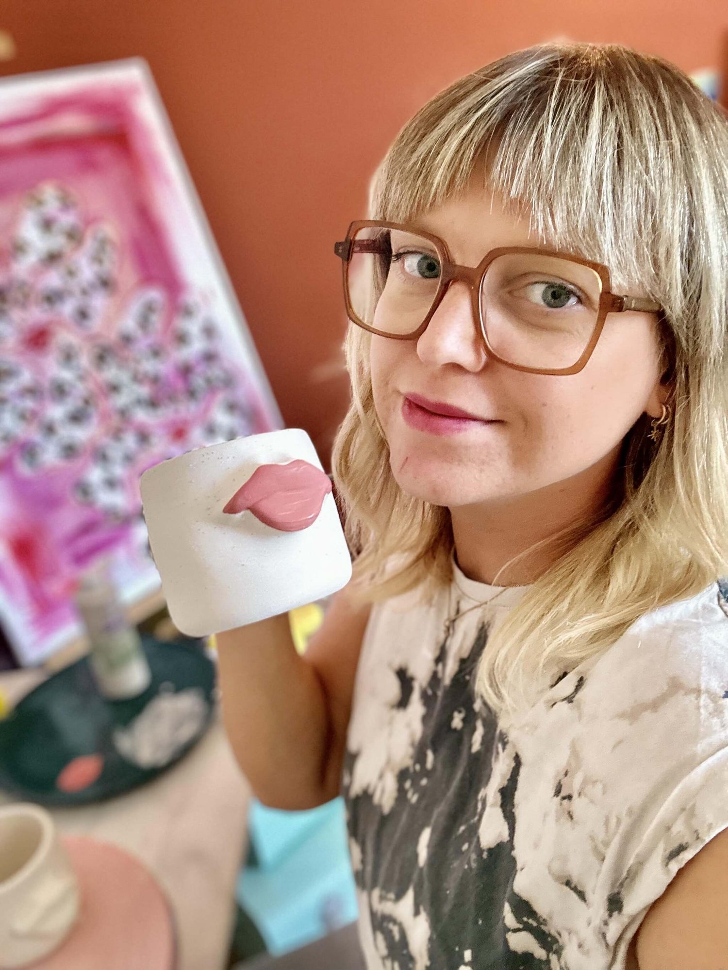 femme avec des lunettes qui porte un mug en céramique avec une bouche rose dessus