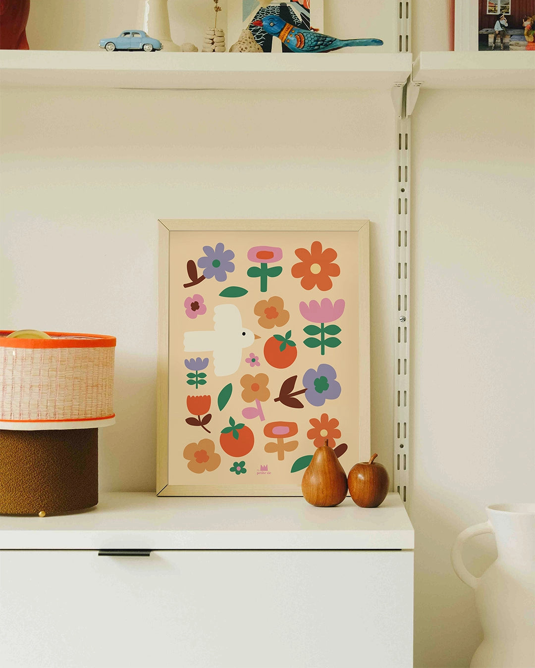 Affiche murale décorative avec un oiseau, des fleurs et des tomates, posée sur un meuble blanc.