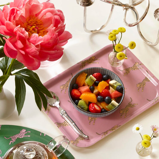 Plateau rectangulaire en bois rose avec des léopards et un bol rempli de fruits.