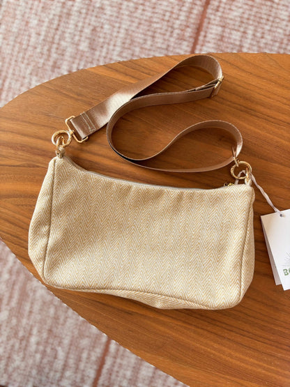 Sac baguette beige en coton, avec une sangle mordorée réglable.