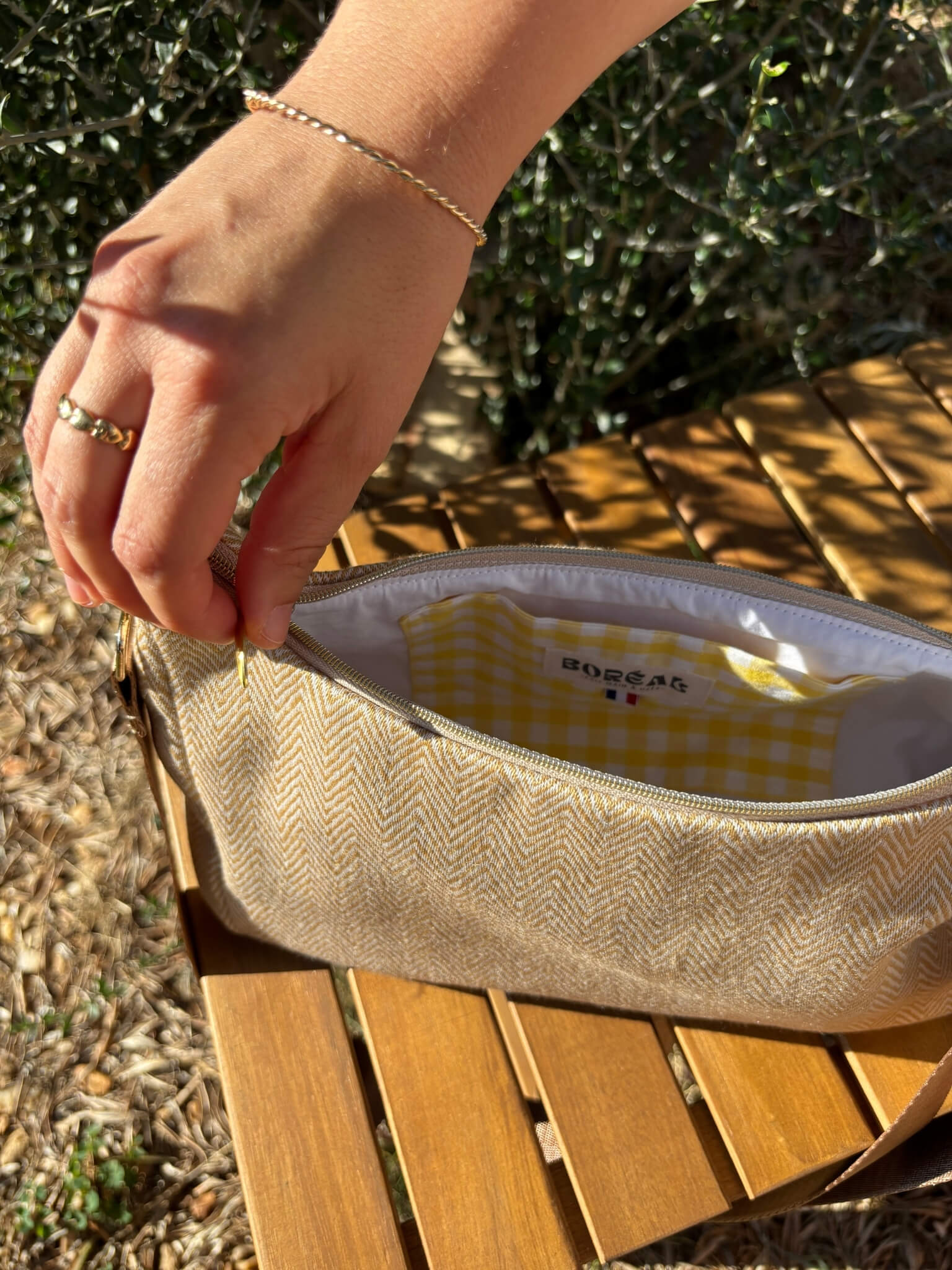 Sac baguette beige en coton, avec une sangle mordorée réglable.