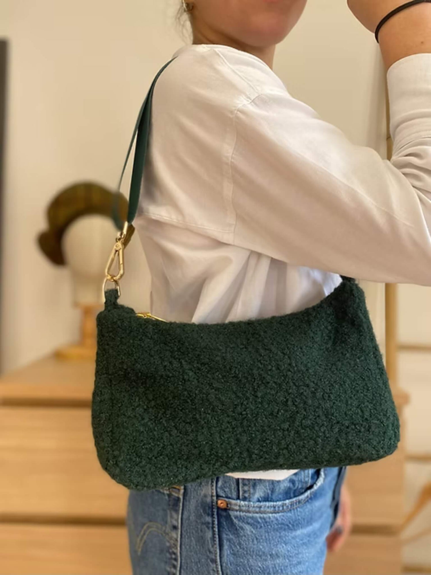 Sac baguette en moumoute verte porté par une femme en chemise blanche.