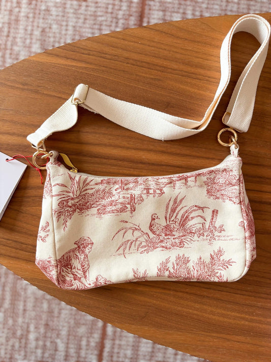 Sac baguette en toile de Jouy rouge, avec une sangle beige réglable.