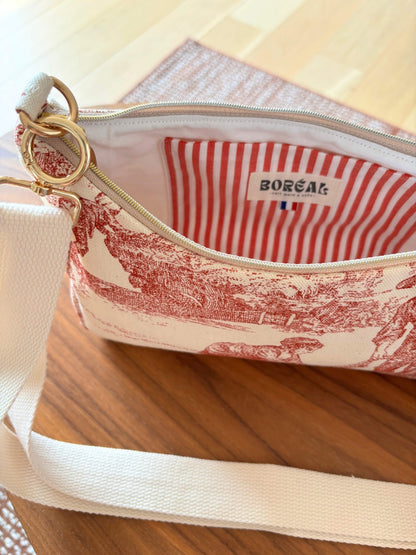 Sac baguette en toile de Jouy rouge, avec une sangle beige réglable.