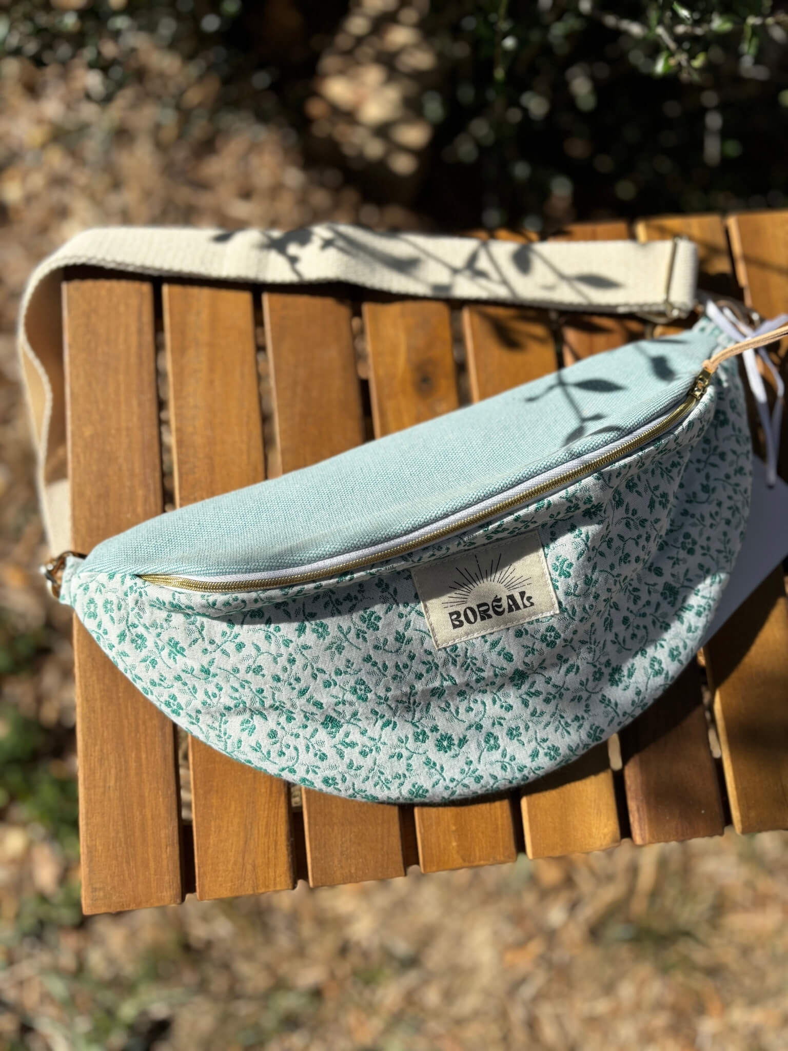 Sac banane bleu en coton imprimé fleuri, avec une sangle beige réglable.