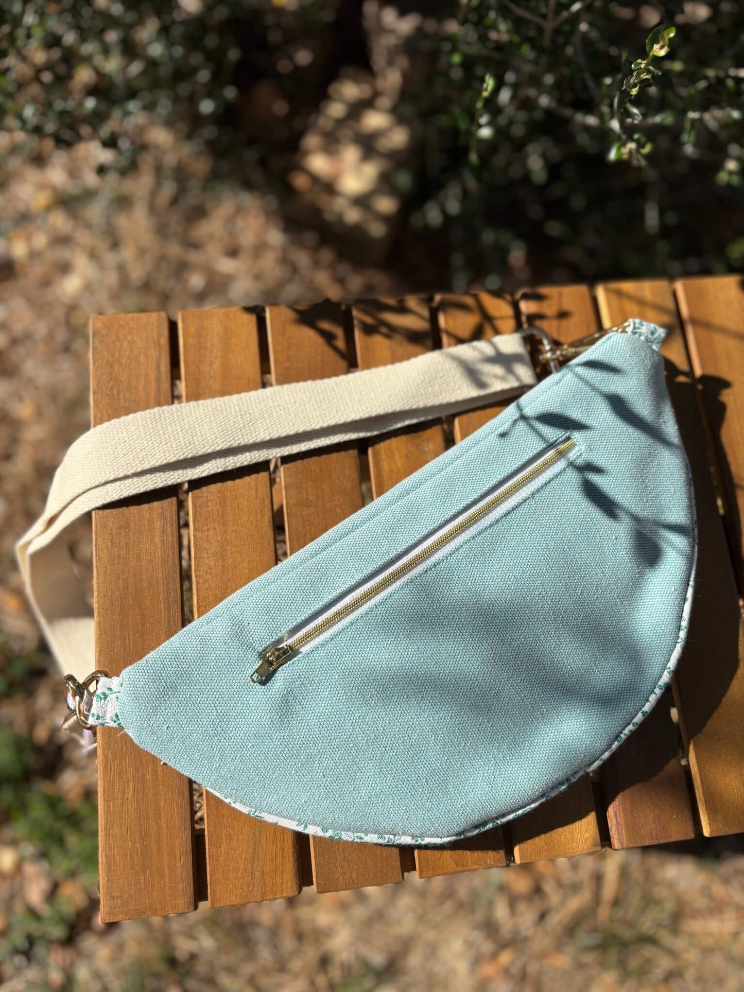Sac banane bleu en coton imprimé fleuri, avec une sangle beige réglable.