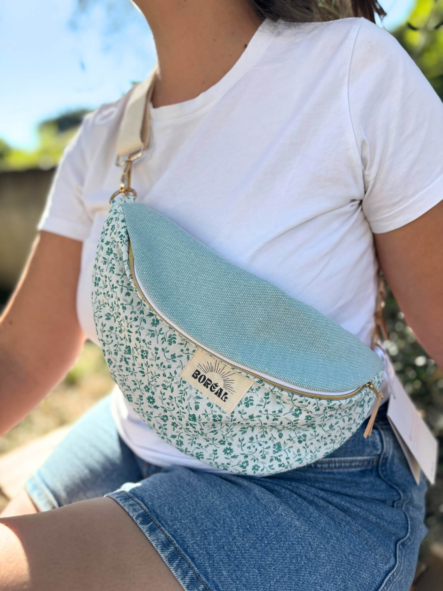 Sac banane bleu en coton imprimé fleuri, avec une sangle beige réglable.