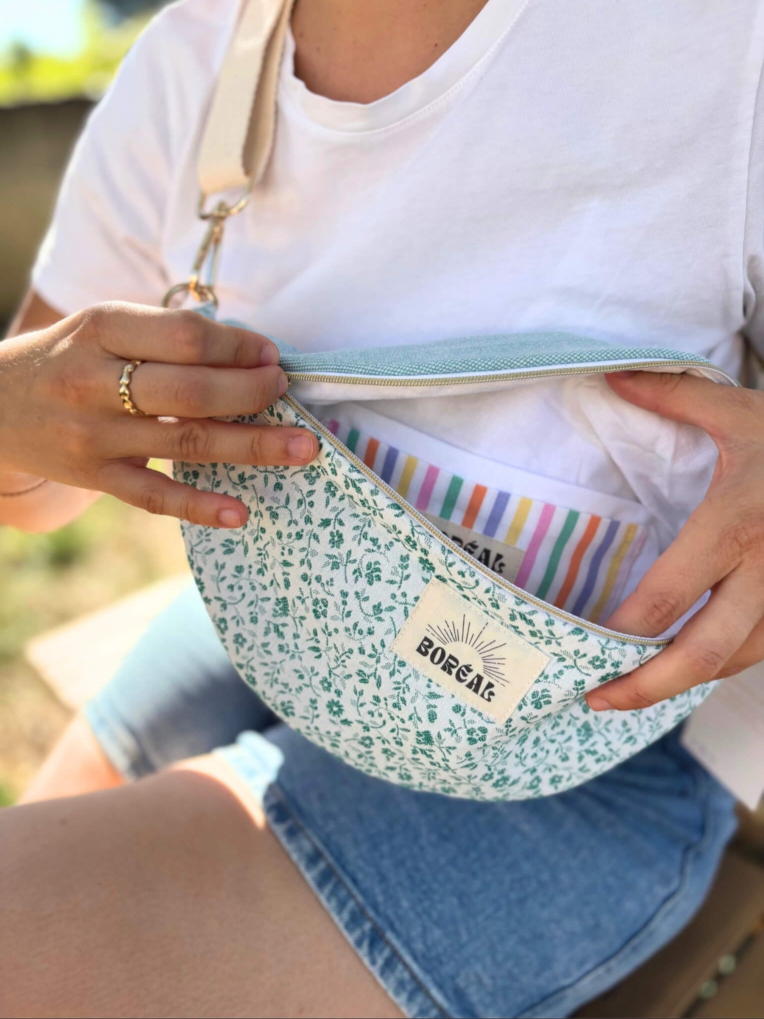 Sac banane bleu en coton imprimé fleuri, avec une sangle beige réglable.