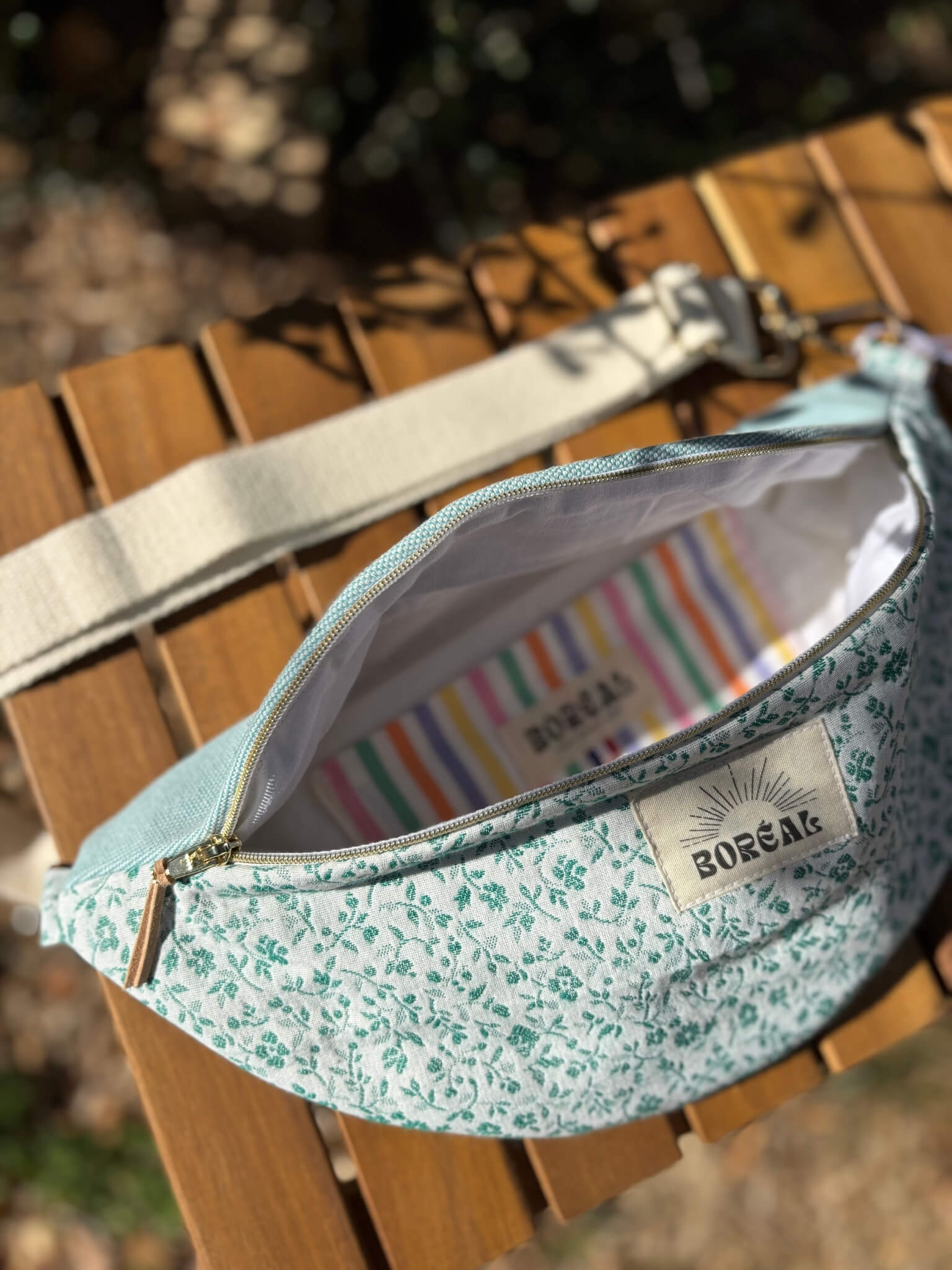 Sac banane bleu en coton imprimé fleuri, avec une sangle beige réglable.