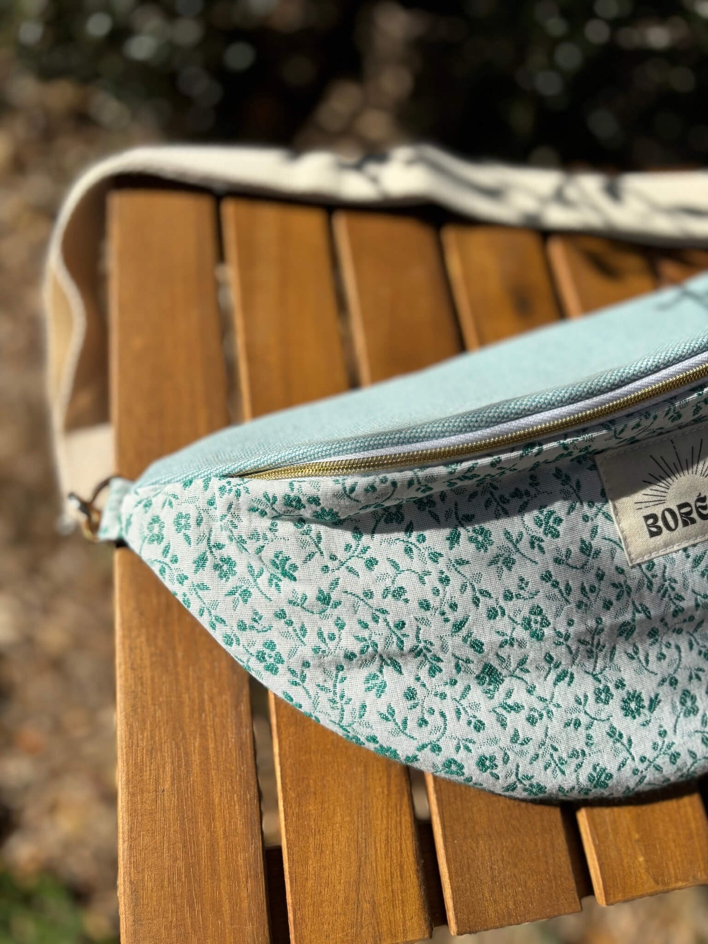 Sac banane bleu en coton imprimé fleuri, avec une sangle beige réglable.