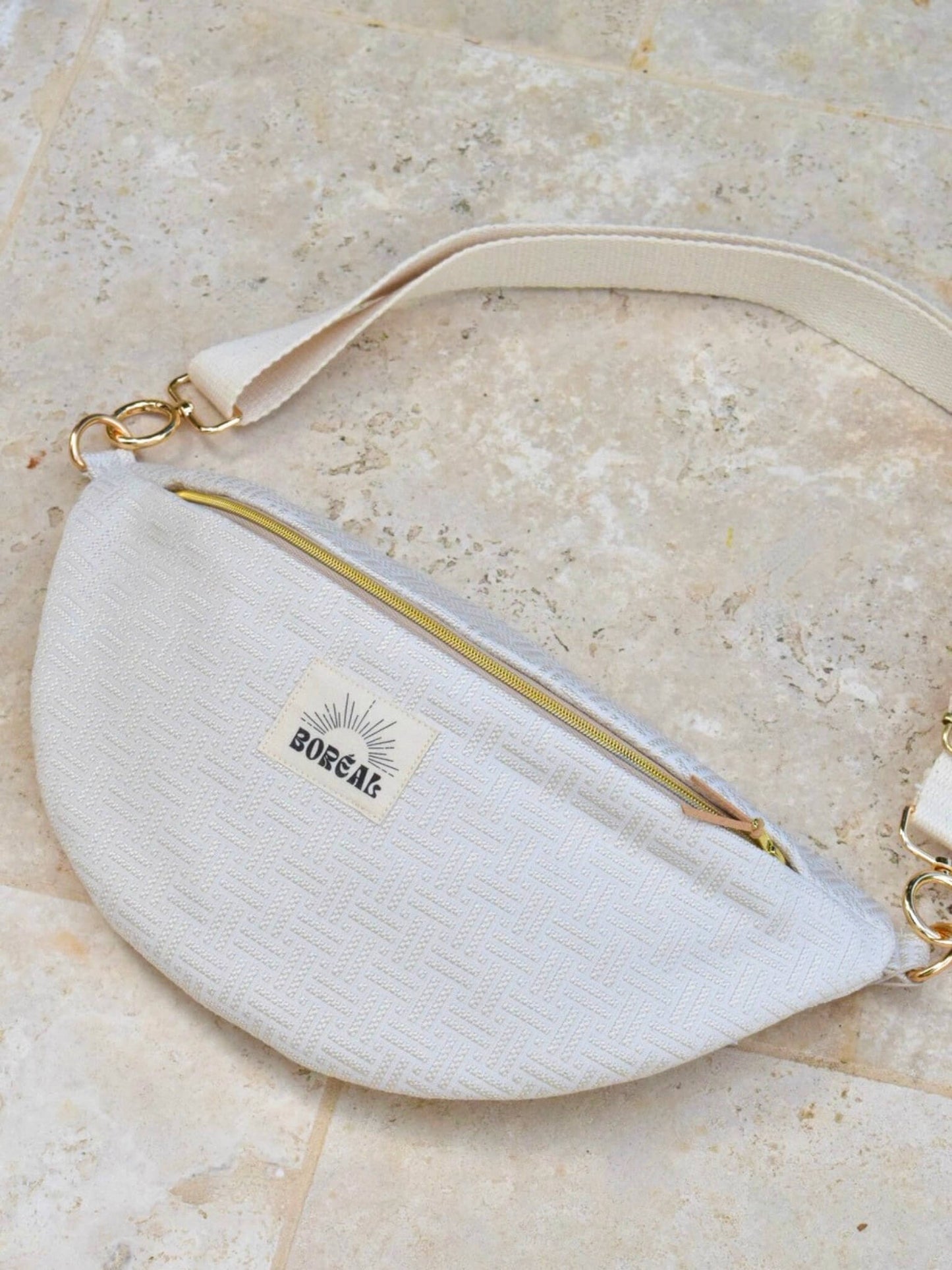Sac banane écru en coton, avec une sangle beige réglable.