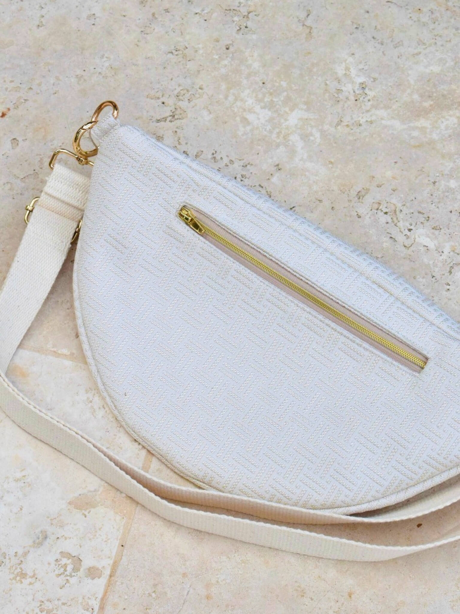 Sac banane écru en coton, avec une sangle beige réglable.