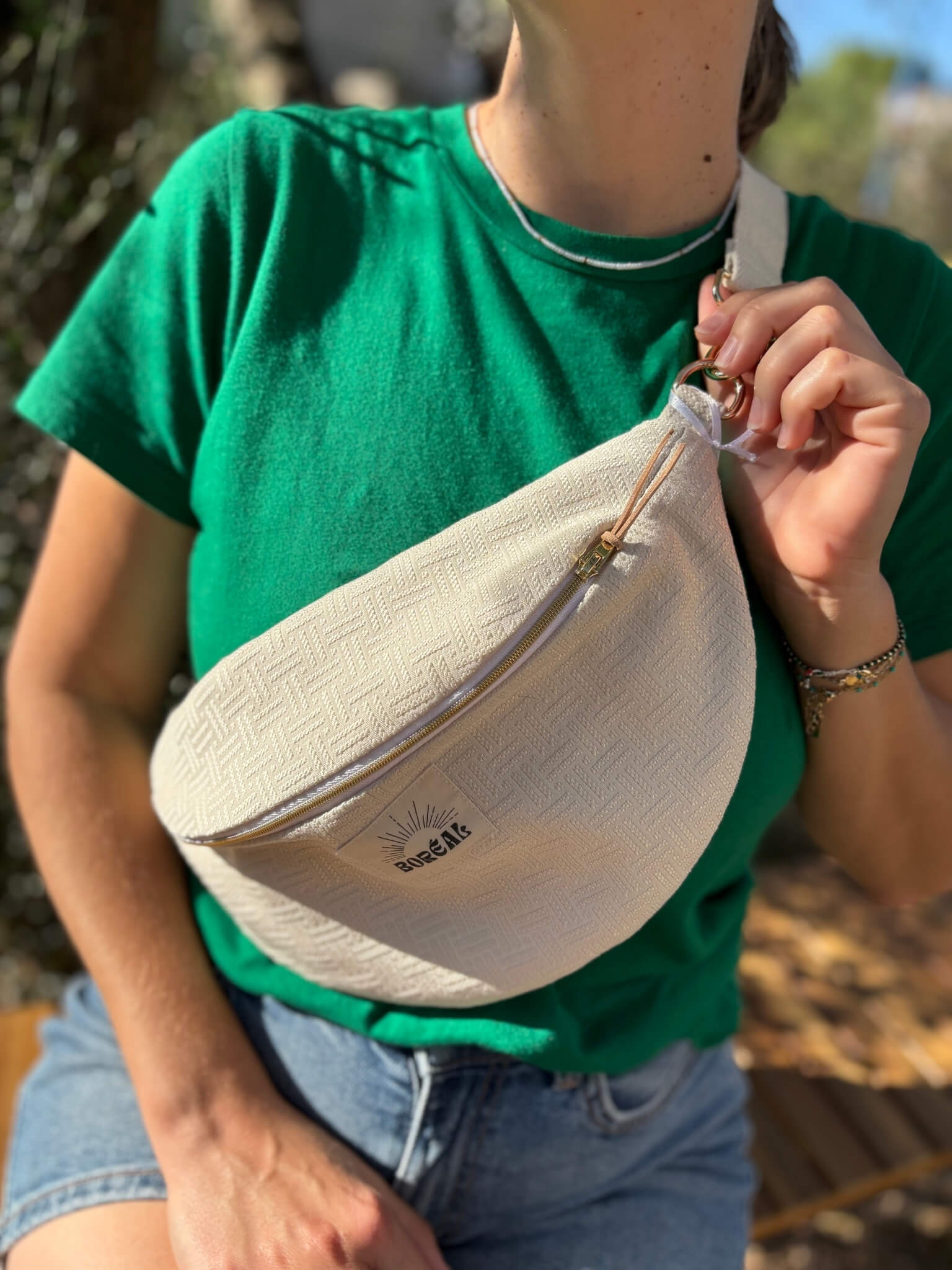 Sac banane écru en coton, avec une sangle beige réglable.