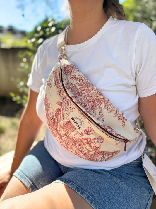 Sac banane en toile de Jouy rouge, avec une sangle beige réglable.