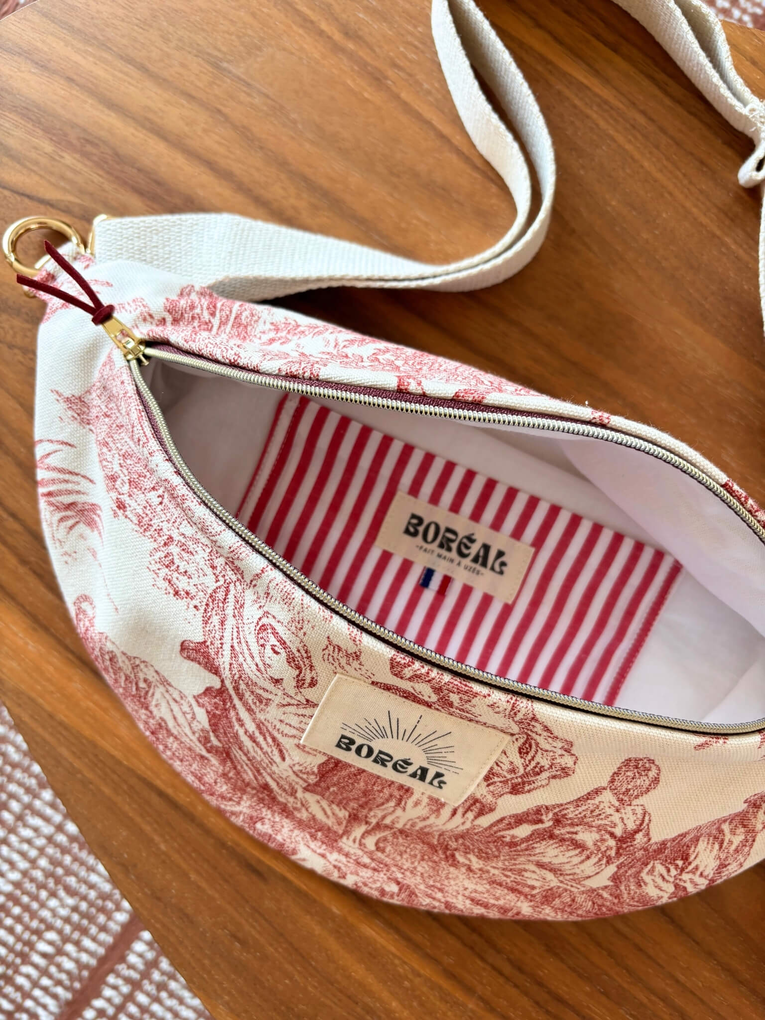 Sac banane en toile de Jouy rouge, avec une sangle beige réglable.