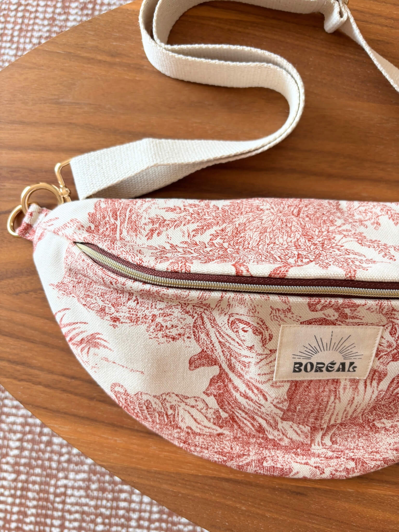 Sac banane en toile de Jouy rouge, avec une sangle beige réglable.