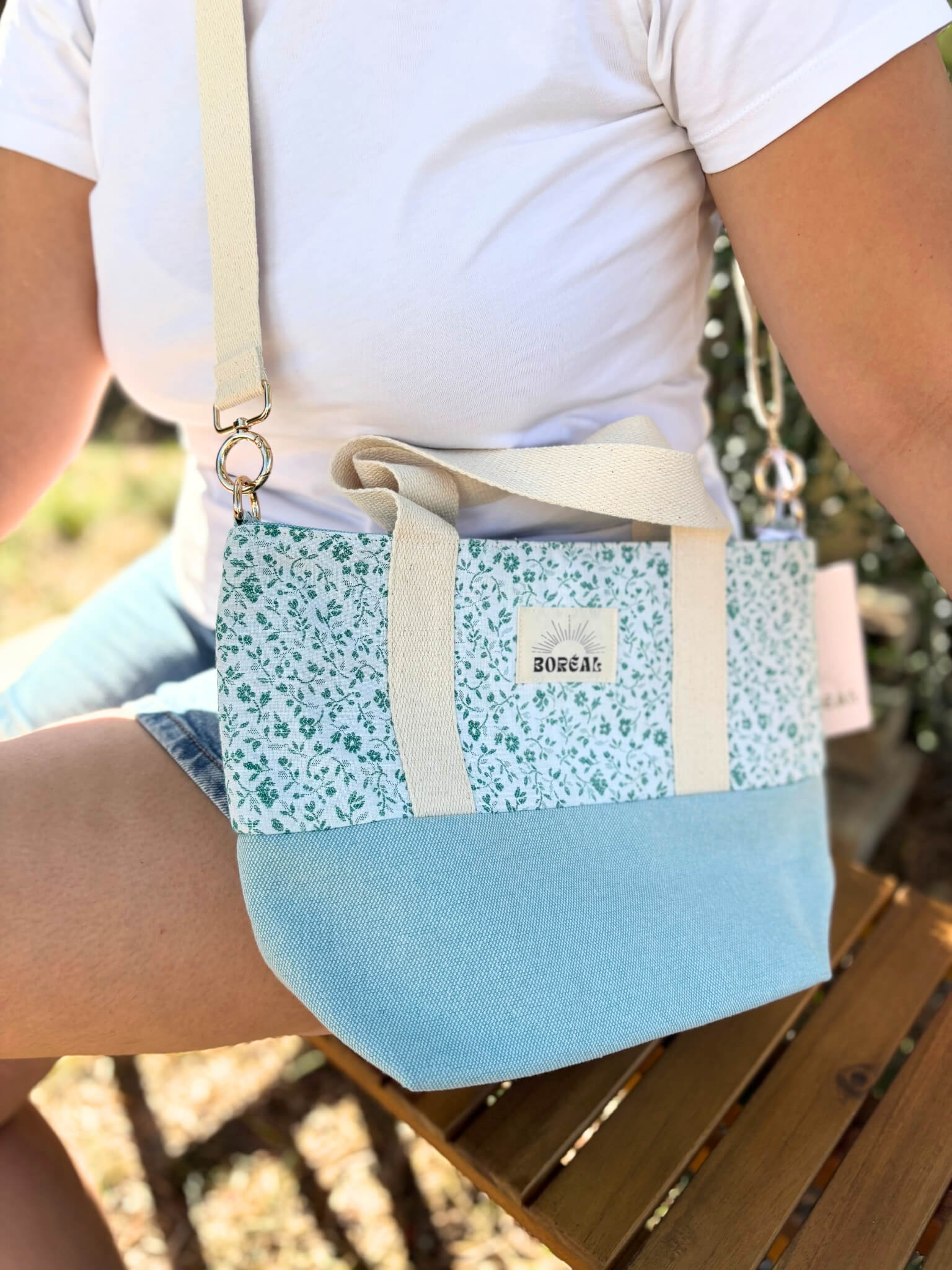 Sac à bandoulière en coton bleu fleuri, avec une sangle beige réglable.