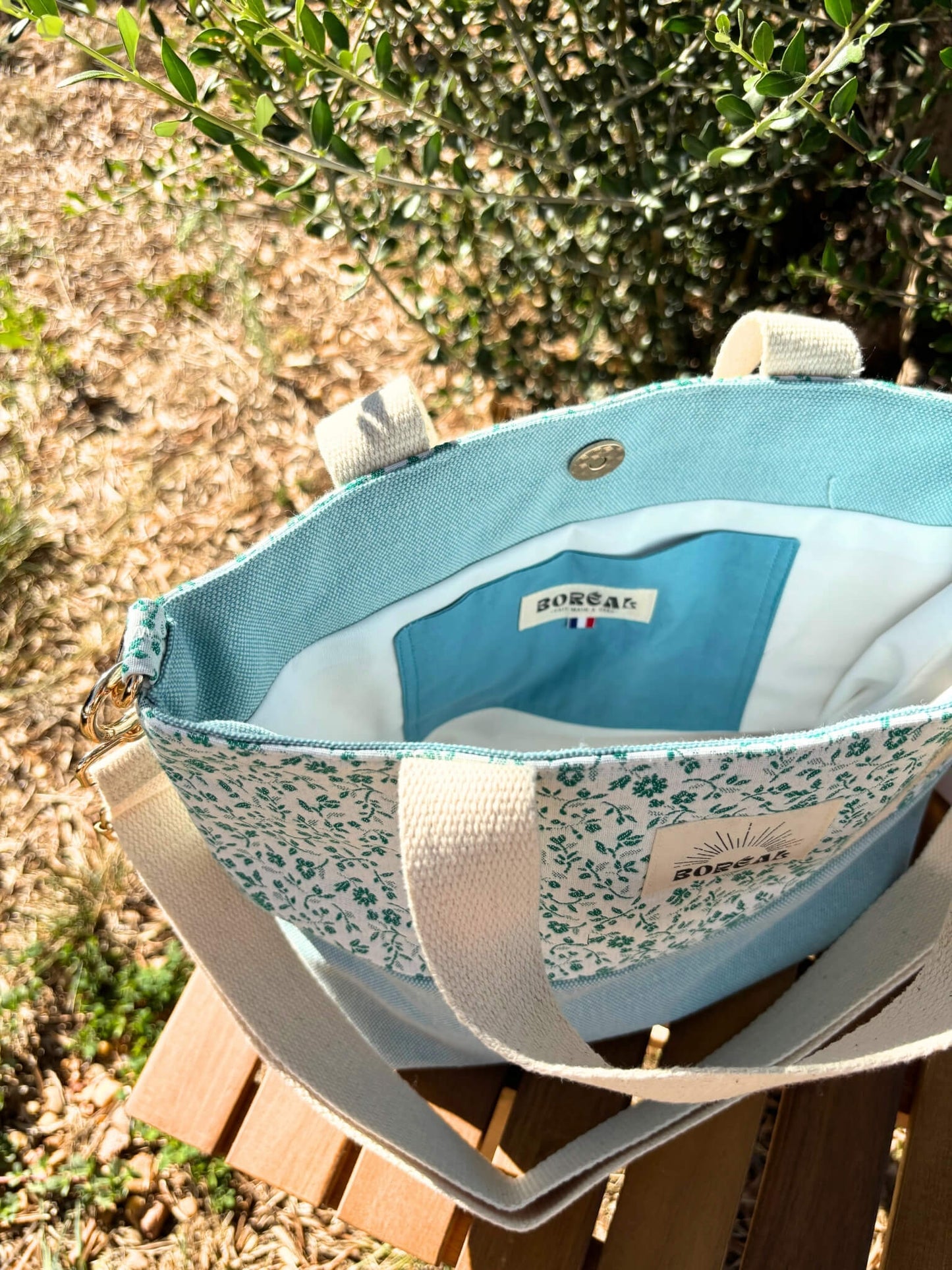 Sac à bandoulière en coton bleu fleuri, avec une sangle beige réglable.