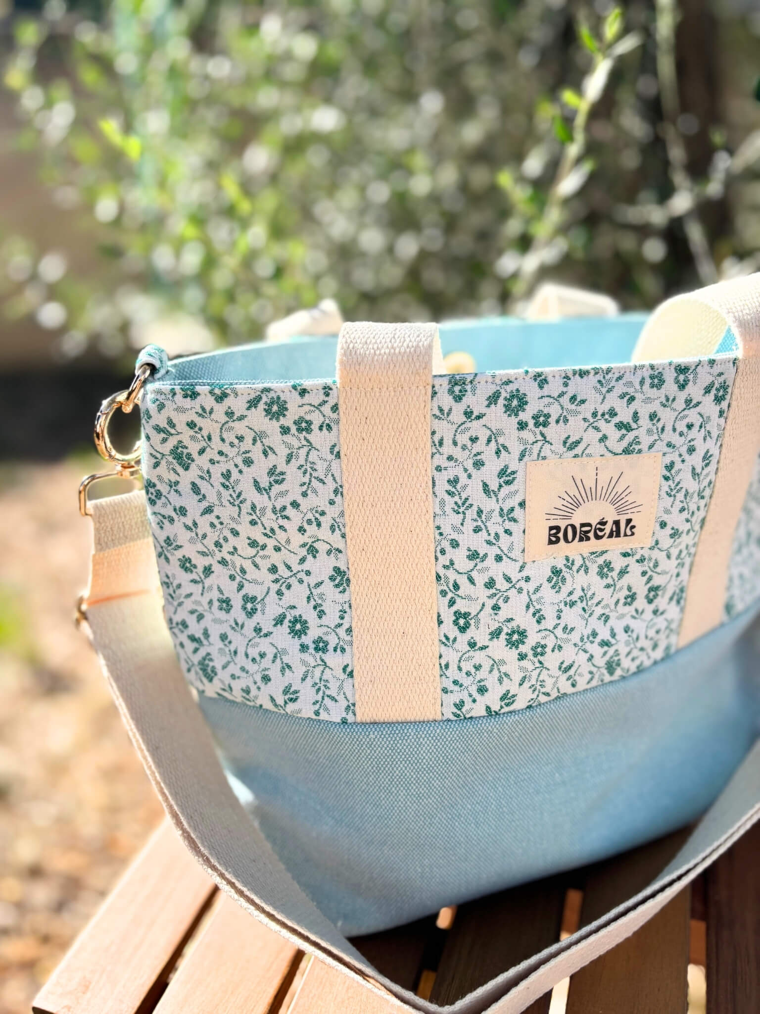 Sac à bandoulière en coton bleu fleuri, avec une sangle beige réglable.